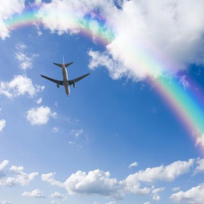 A Jetliner Aeroplane Flying Over White Clouds Towards A Rainbow In Blue Sky